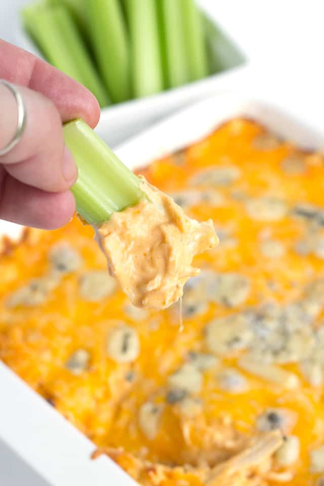 piece of celery being dipped into warm Buffalo chicken dip