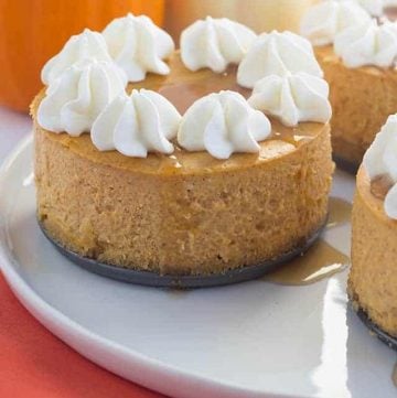 Three mini pumpkin cheesecakes topped with whipped cream on a plate.