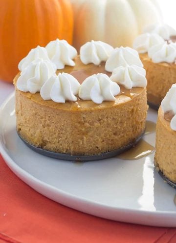 Mini Pumpkin Cheesecakes topped with maple syrup and whipped cream, sitting on a dessert platter