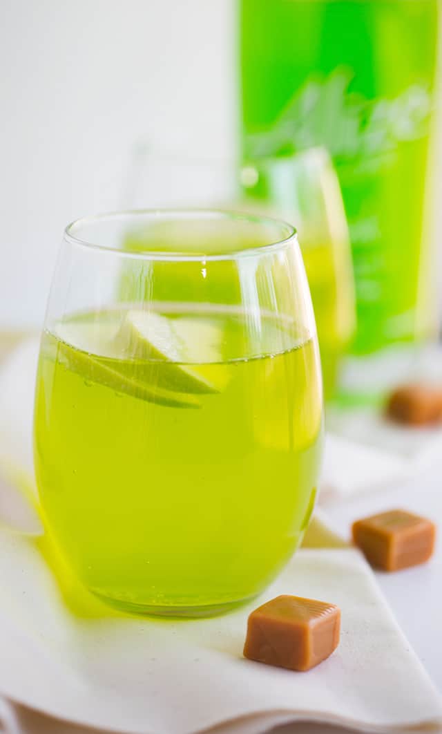 Caramel Apple Cocktail - how fun is a bright green drink that's caramel apple flavored?! This is a sweet cocktail that packs a punch from the liqueur. Garnish with a couple of apple slices and serve at your next party!