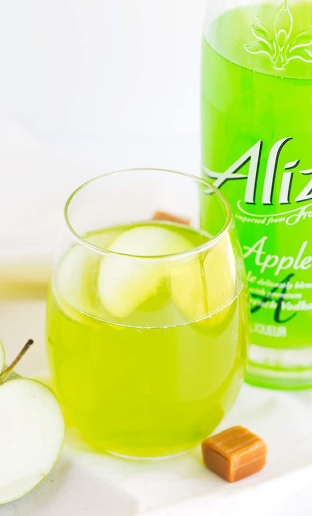 Caramel Apple Cocktail - how fun is a bright green drink that's caramel apple flavored?! This is a sweet cocktail that packs a punch from the liqueur. Garnish with a couple of apple slices and serve at your next party!