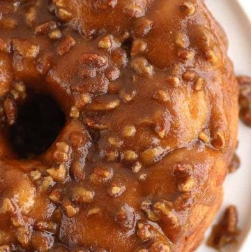 A Pecan Pie bundt cake with caramel and pecans on a plate.