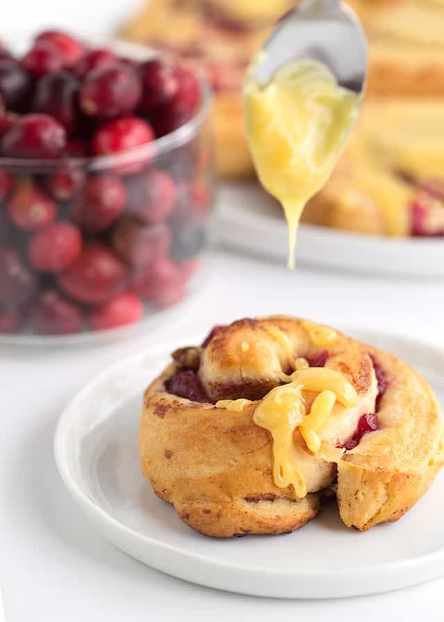 one cranberry orange cinnamon roll with an orange glaze being drizzled on top.