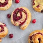 Freshly baked cranberry orange cinnamon rolls sitting on baking sheet and parchment paper.