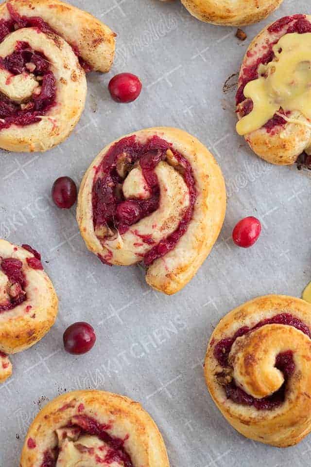 Freshly baked cranberry orange cinnamon rolls sitting on baking sheet and parchment paper.