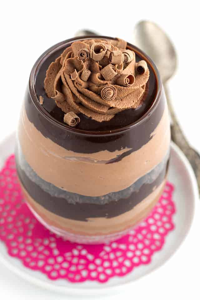 Close up of a glass filled with layers of chocolate trifle on a pink doily and white saucer