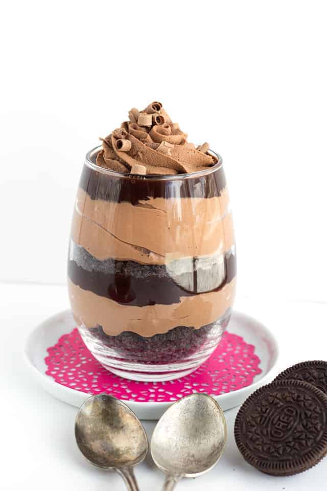 Eye level shot of a glass filled with layers of chocolate trifle on a pink doily and white saucer