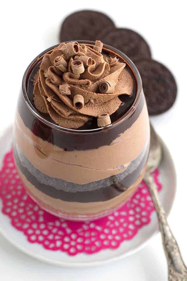 Close up of a glass filled with layers of chocolate trifle on a pink doily and white saucer