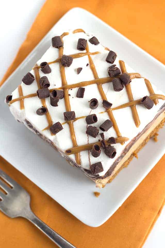 Slice of the cookie butter layer dessert on a small white square dessert plate with an orange cloth photo taken from above the slice