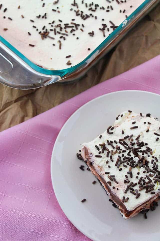 Overhead picture of a square of chocolate layer dessert on a white plate with a pink napkin underneath it. 