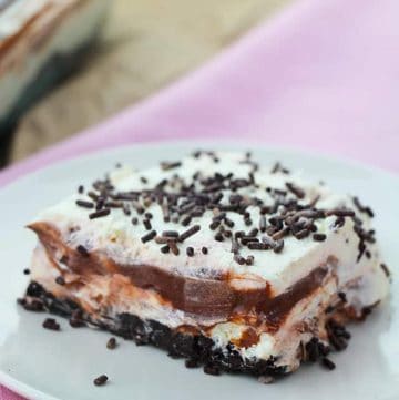 A square of chocolate layer dessert on a white plate with a pink napkin