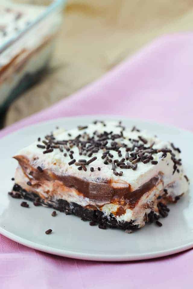 A square of chocolate layer dessert on a white plate with a pink napkin