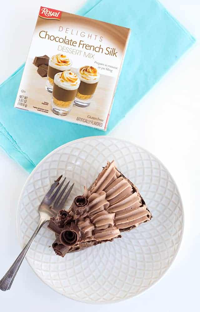 overhead shot of a slice of the chocolate cream pie on a white plate with a box of Royal Delights dessert mix sitting on a piece of blue fabric beside it.