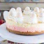 A pink and white strawberries and cream cheesecake on a white plate.
