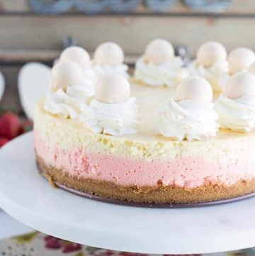 A pink and white strawberries and cream cheesecake on a white plate.