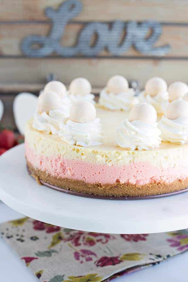 Full strawberries and cream cheesecake sitting on a marble cake stand