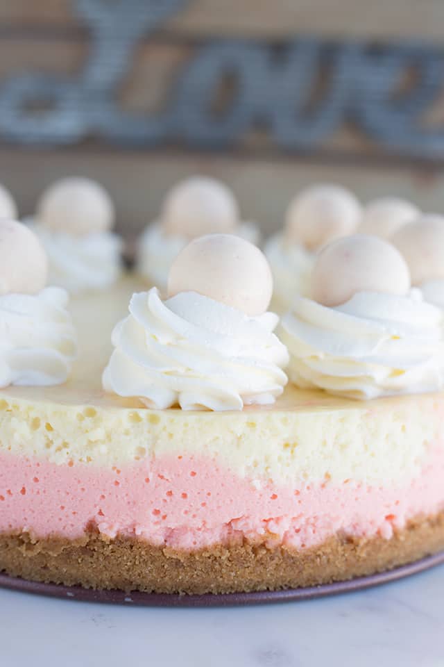 Strawberries and Cream Cheesecake - This cheesecake is packed full of flavor! There's a cookie crust, pink strawberry cheesecake layer, vanilla cheesecake layer, strawberries and cream truffles baked inside the cheesecake and topped with whipped cream and more strawberries and cream truffles! This is the perfect Valentine's Day cheesecake! #cookiedoughandovenmitt #cheesecake #cheesecakerecipes #dessertrecipes #strawberries Full strawberries and cream cheesecake sitting on a marble cake stand