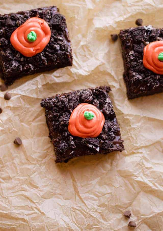 Three carrot patch brownies with orange frosting on a piece of paper.