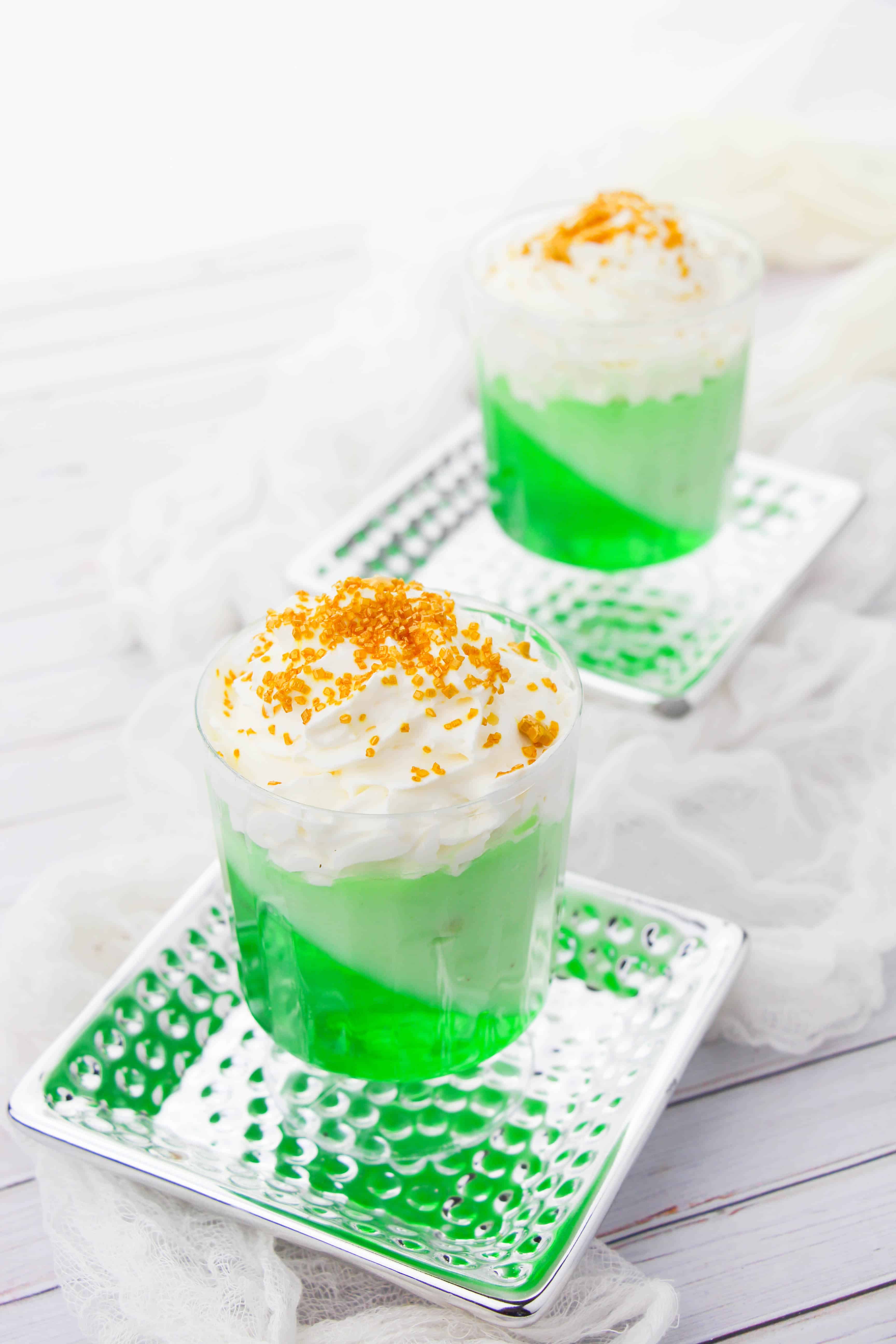 Two green jello parfaits each sitting on a silver reflective plate