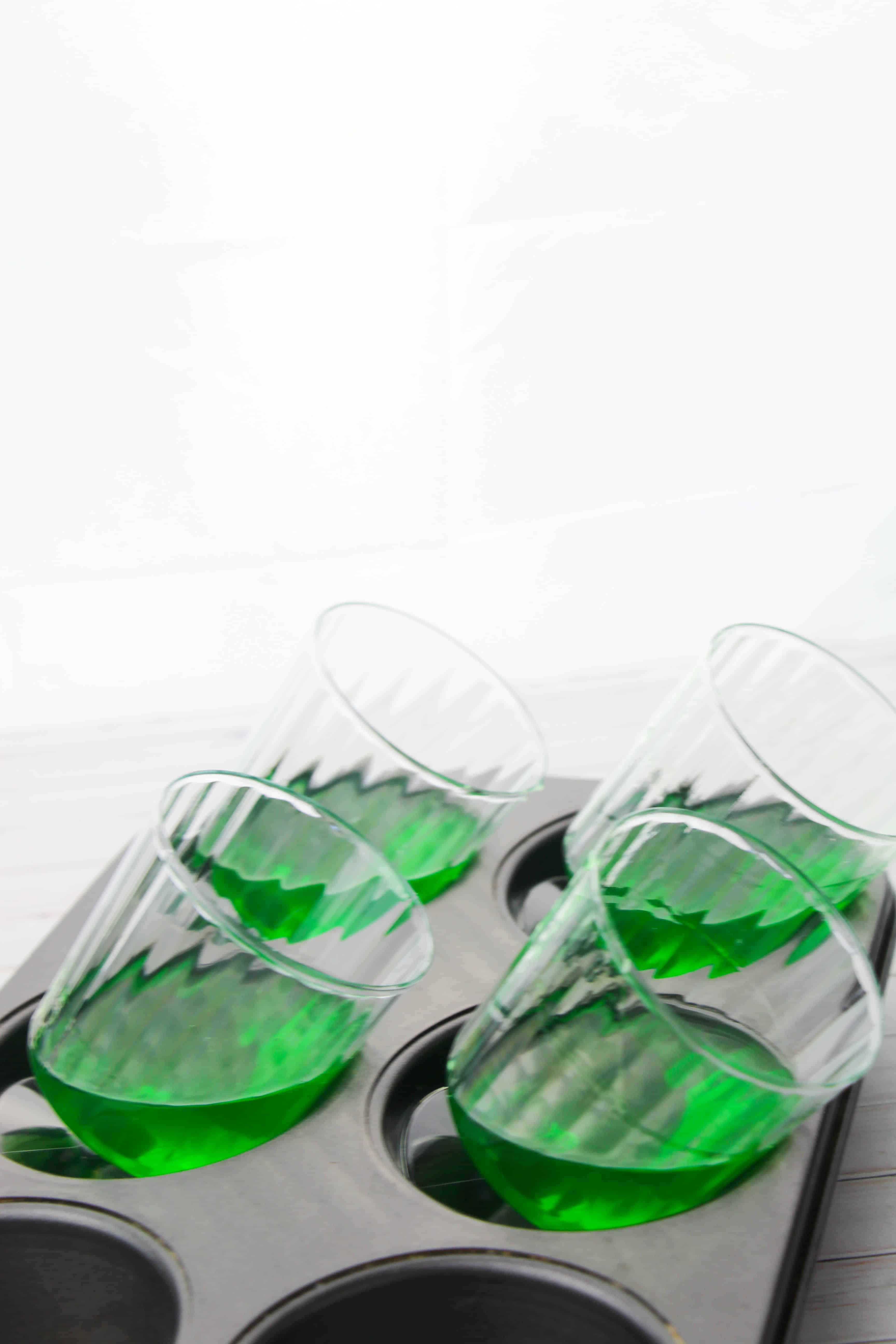 A photo of the glasses tipped to the side in a muffin pan with green jello setting up in them.