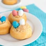 Three easter nests on a plate with blue and yellow eggs filled with malted milk candies.