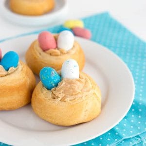 Three easter nests on a plate with blue and yellow eggs filled with malted milk candies.