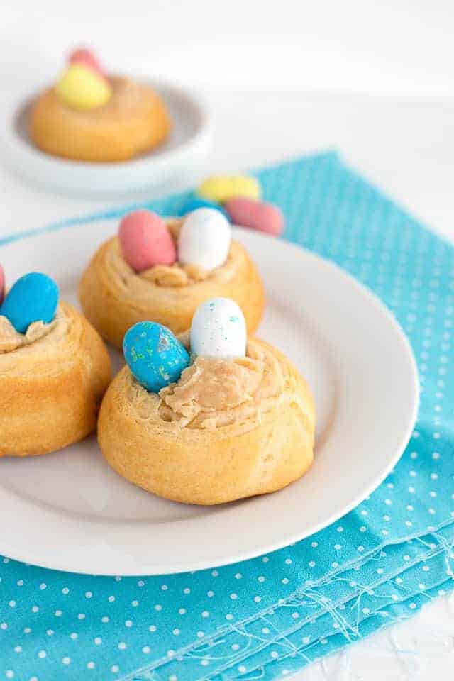 Three easter nests on a plate with blue and yellow eggs filled with malted milk candies.