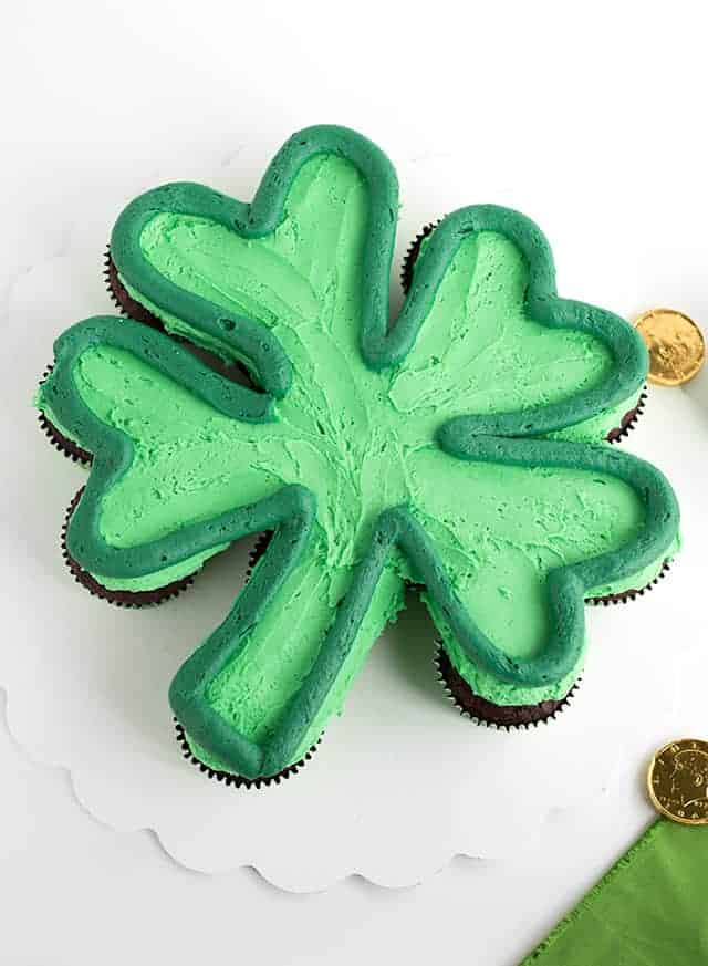 Shot at a 90 degree angle green shamrock cupcake cake with a dark green outline on a white cake board with gold chocolate coins scattered.