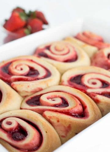 Strawberry sweet rolls in a white baking dish with strawberries in the background.