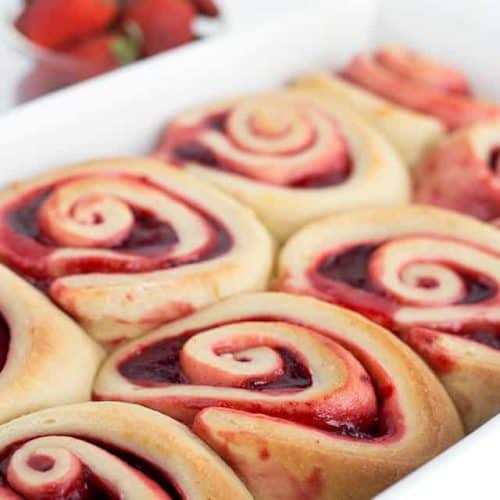 Strawberry sweet rolls in a white baking dish with strawberries in the background.
