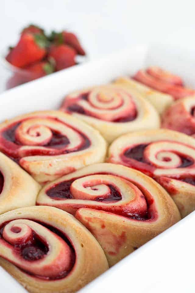 Strawberry sweet rolls in a white baking dish with strawberries in the background.