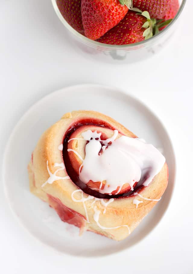 A strawberry sweet roll on a small white dish with glaze drizzled on top.