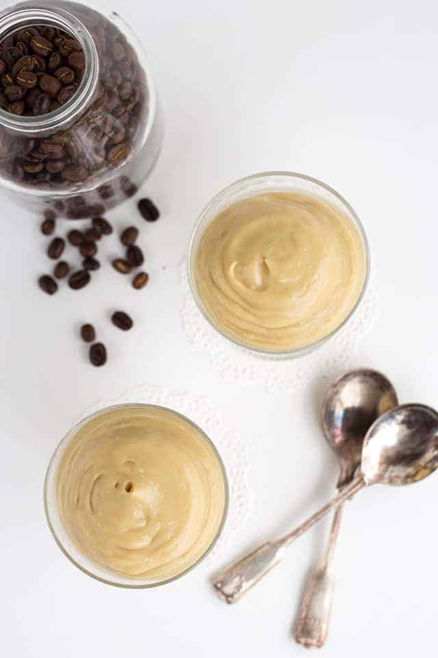 overhead shot of two cups of coffee pudding with coffee beans and two spoons