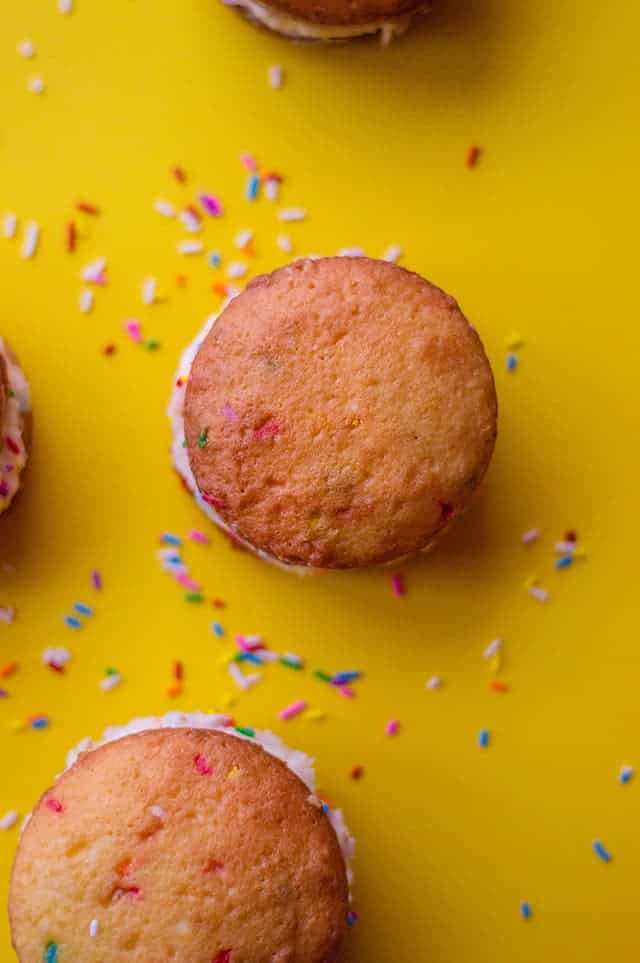 overhead of funfetti cake mix whoopie pies with yellow background and sprinkles scattered