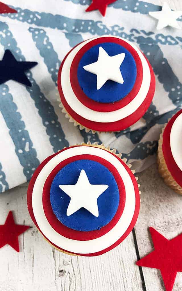 two 4th of july cupcakes close up with red and blue stars and a blue and white fabric in the background