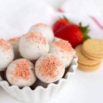 A white bowl filled with strawberry shortcake truffles and chocolate covered cookies.