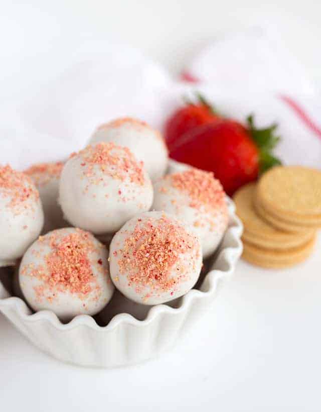 A white bowl filled with strawberry shortcake truffles and chocolate covered cookies.