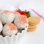 Half of the white bowl of strawberry shortcake truffles in the picture with a white and red hand towel and ingredients behind them