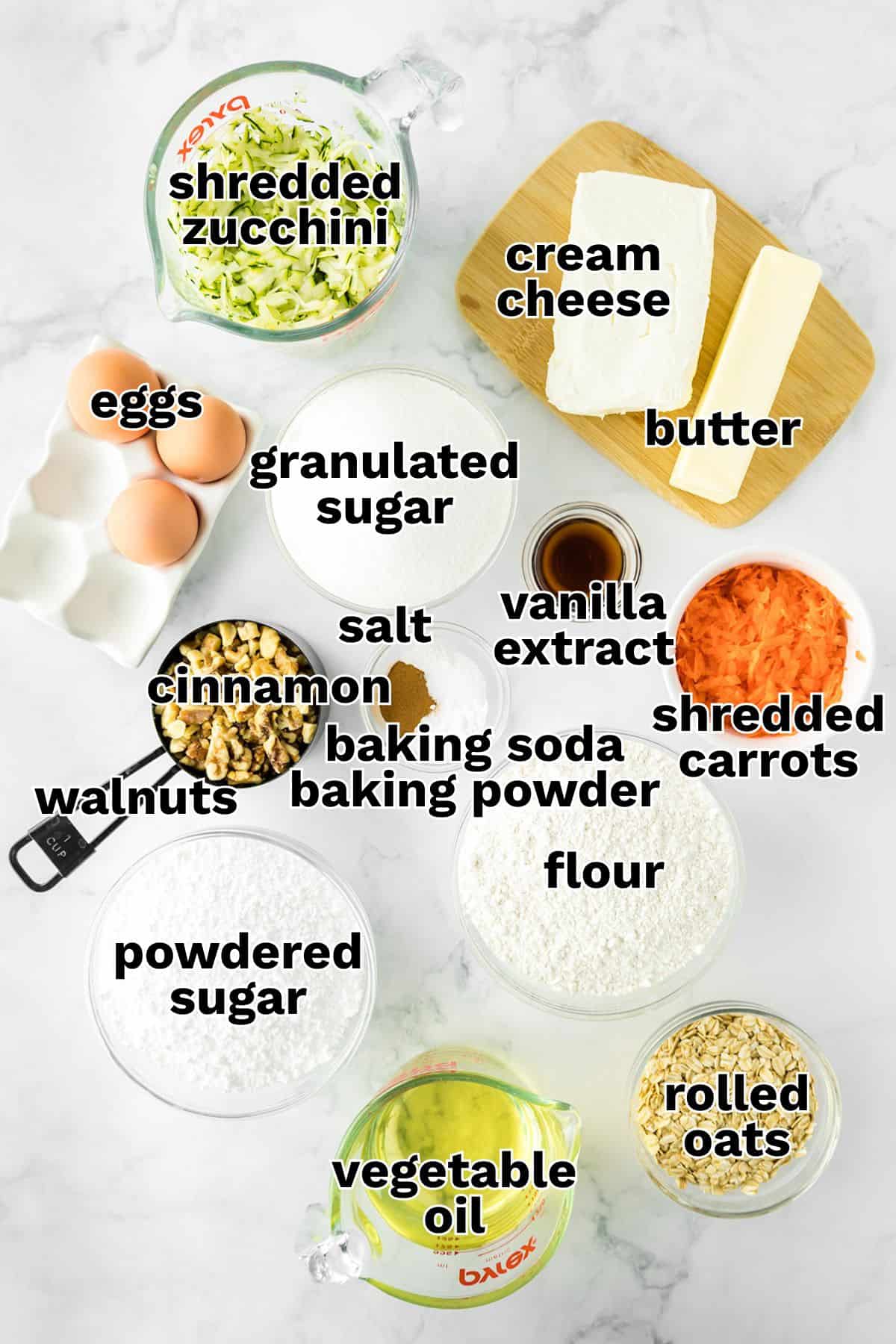 Ingredients for zucchini carrot bread and zucchini bars, including eggs, shredded zucchini, shredded carrots, walnuts, flour, sugar, butter, cream cheese, oil, oats, and baking essentials, arranged on a white surface.