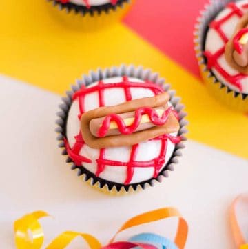 three hot dog cupcakes with a yellow, red, white background