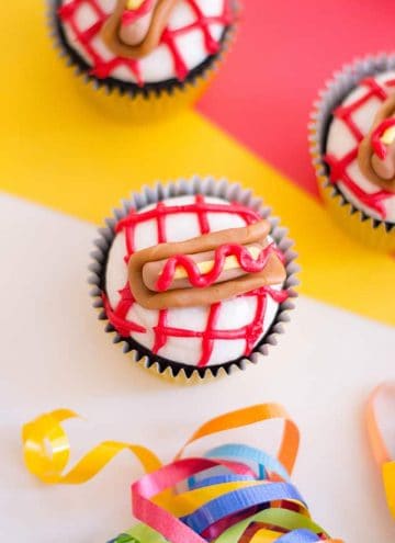 three hot dog cupcakes with a yellow, red, white background