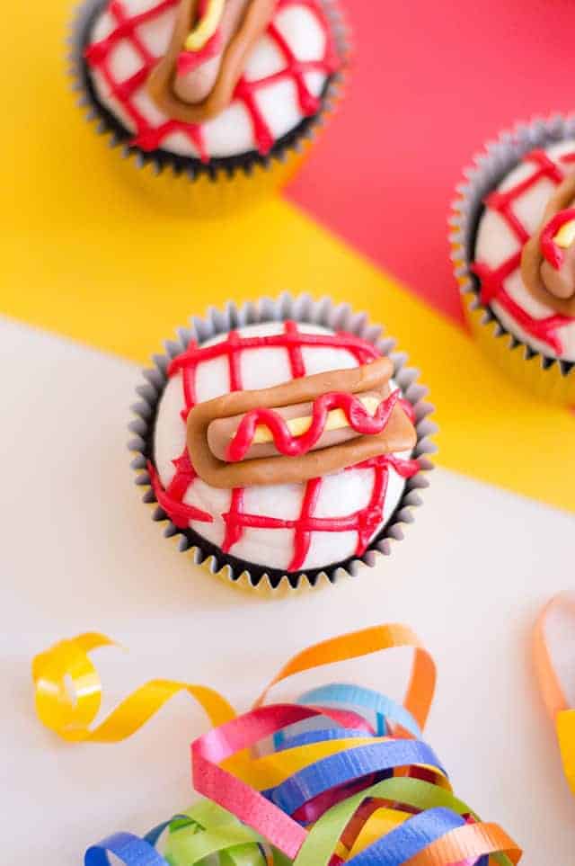 three hot dog cupcakes with a yellow, red, white background