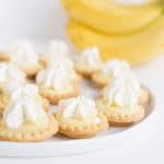 Mini banana cream pies on a white plate with bananas in the background