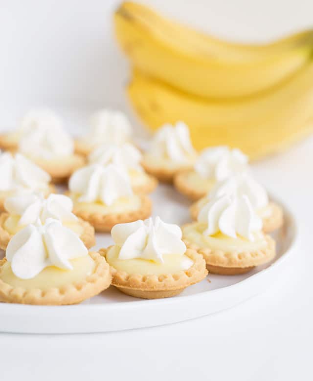 Mini banana cream pies on a white plate with bananas in the background