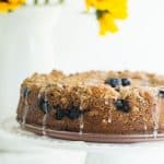 Blueberry Sour Cream Coffee Cake on a cake stand with sunflowers in the background.