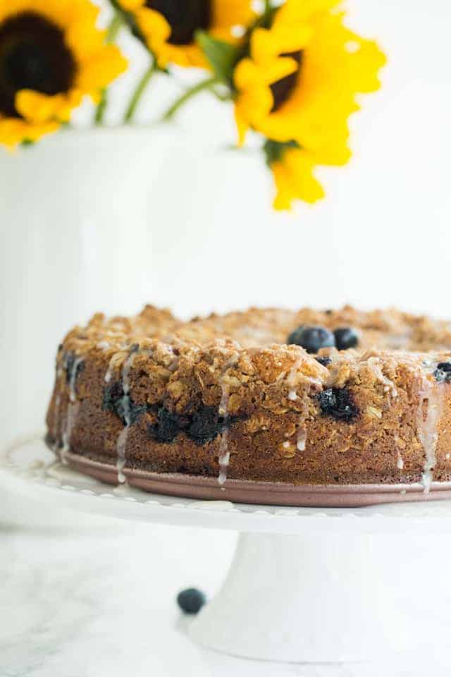 Blueberry Sour Cream Coffee Cake on a cake stand with sunflowers in the background.