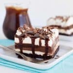 slice of chocolate lasagna with chocolate syrup dripping down the sides on a white plate with a blue napkin under it