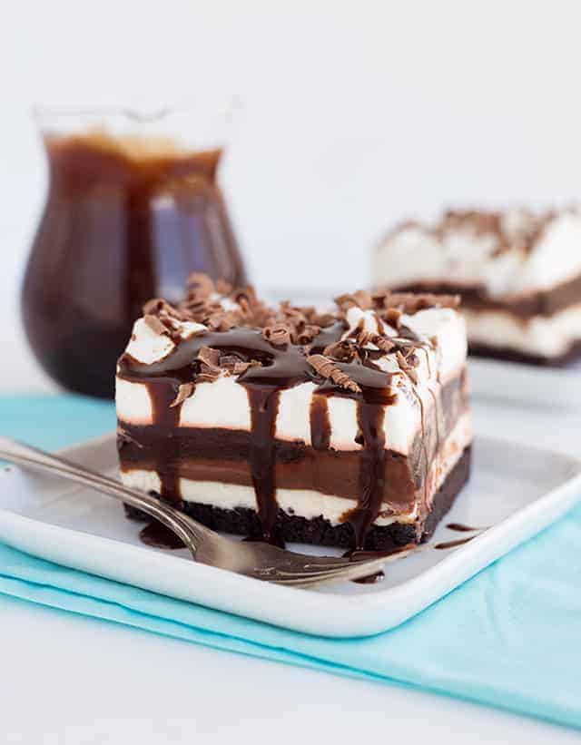 slice of chocolate lasagna with chocolate syrup dripping down the sides on a white plate with a blue napkin under it