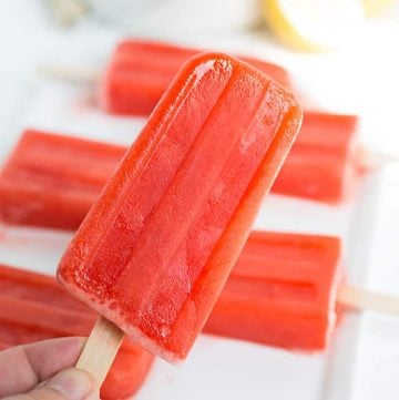 holding a strawberry lemonade popsicle with popsicles on a plate in the background
