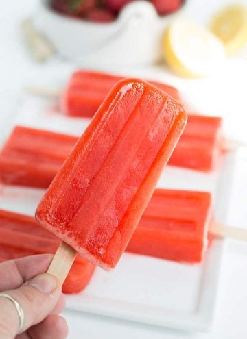 holding a strawberry lemonade popsicle with popsicles on a plate in the background